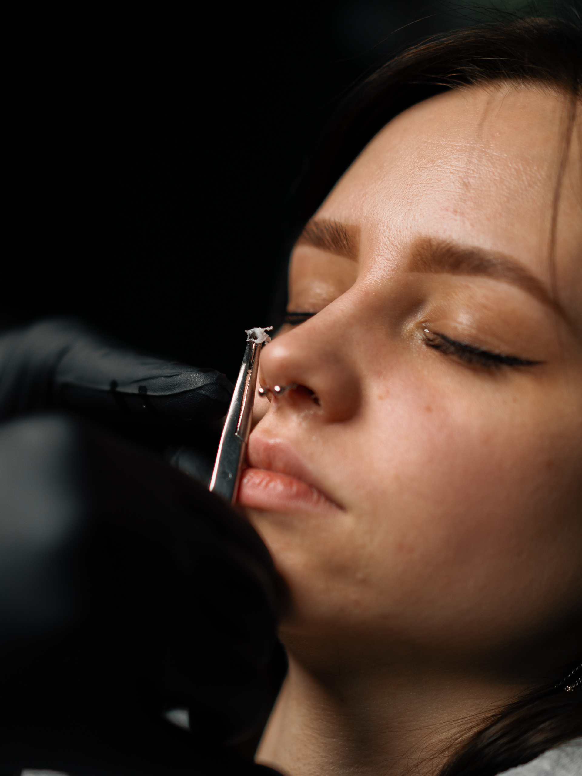 Piercing process Professional nose piercing of girl in disposable black gloves sexy nose ring